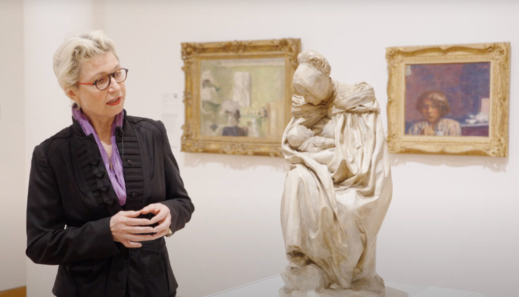 Woman with glasses in a dark suit discusses a terra cotta sculpture in our European Galleries.