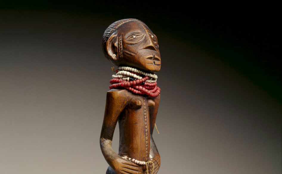 wooden sculpture of a male figure with read and white beads around his neck.