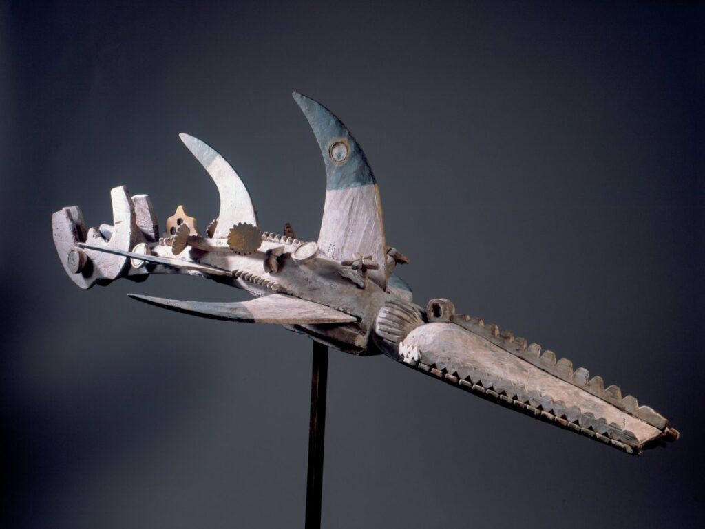 This wooden water spirit headdress combines crocodile teeth and the fins and tail of a large fish, decorated with mirrors and yellow pigment.