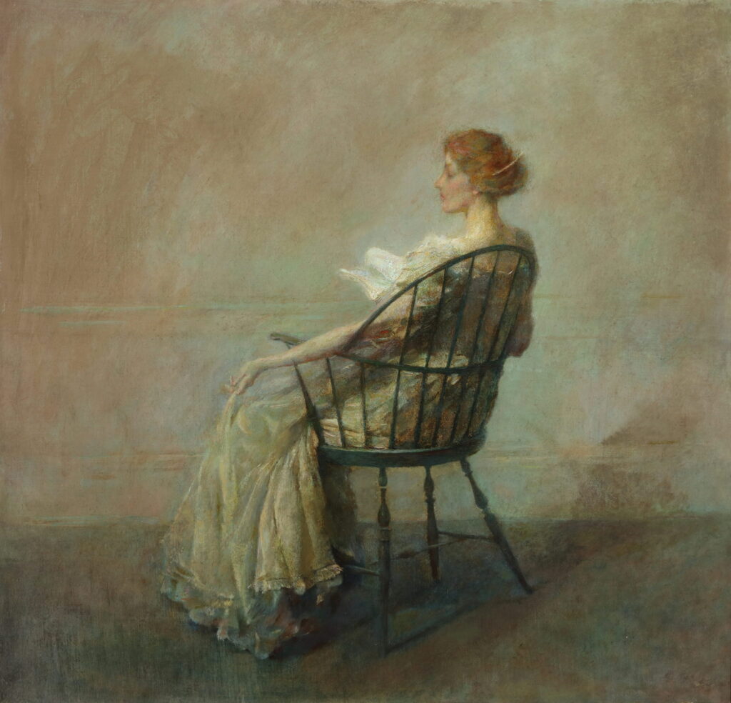 Profile of a red-headed woman, viewed from the back sits in a windsor chair reading a book.