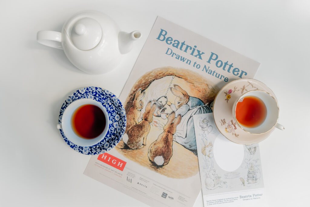 Two tea cups and a tea pot are on a table with Beatrix Potter posters