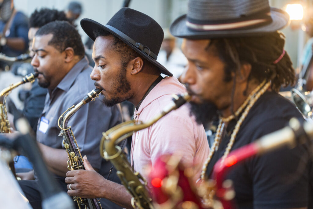three men with brown skin and hats playing the saxaphone.