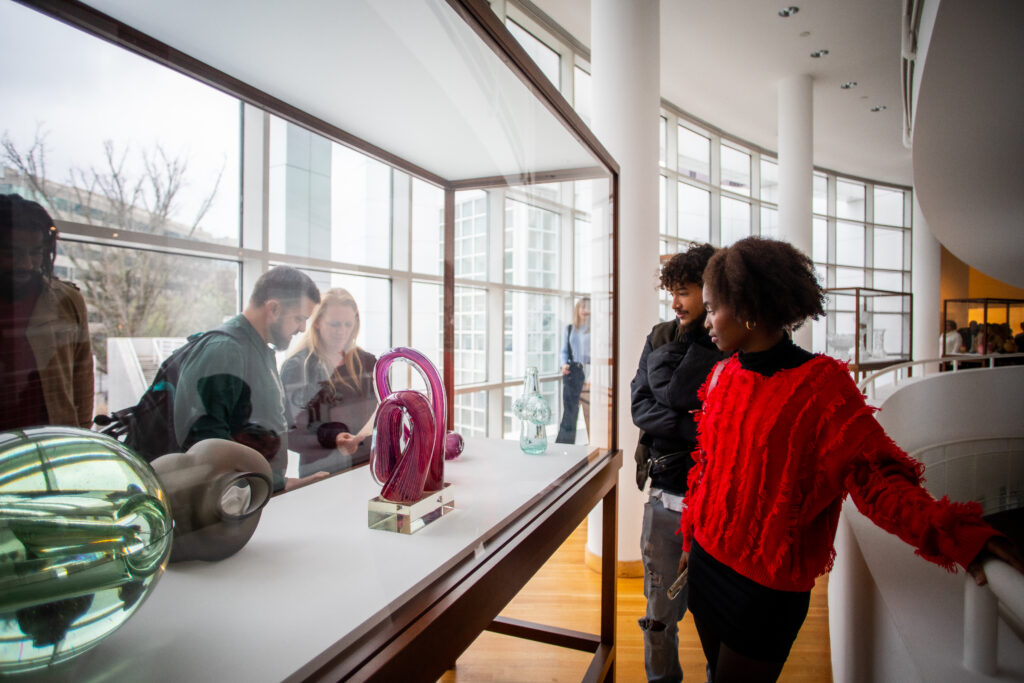Four visitors surround and look at a case that holds glass objects