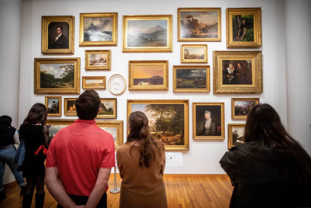 A group of visitors look up at a salon wall gallery of artworks