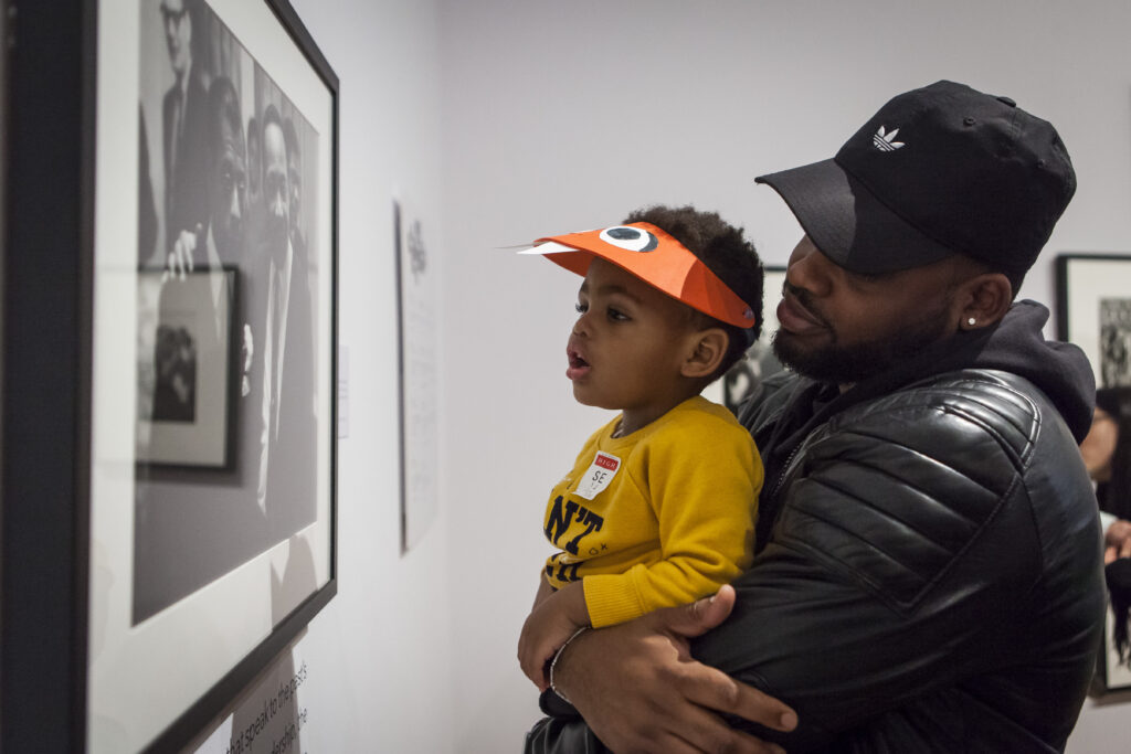Man holds up his young son to look at a photograph hanging in the High Museum.