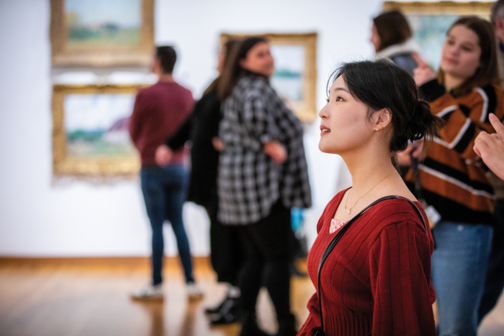Woman of Asian decent in a wine red dress looks at an artwork in the European galleries.